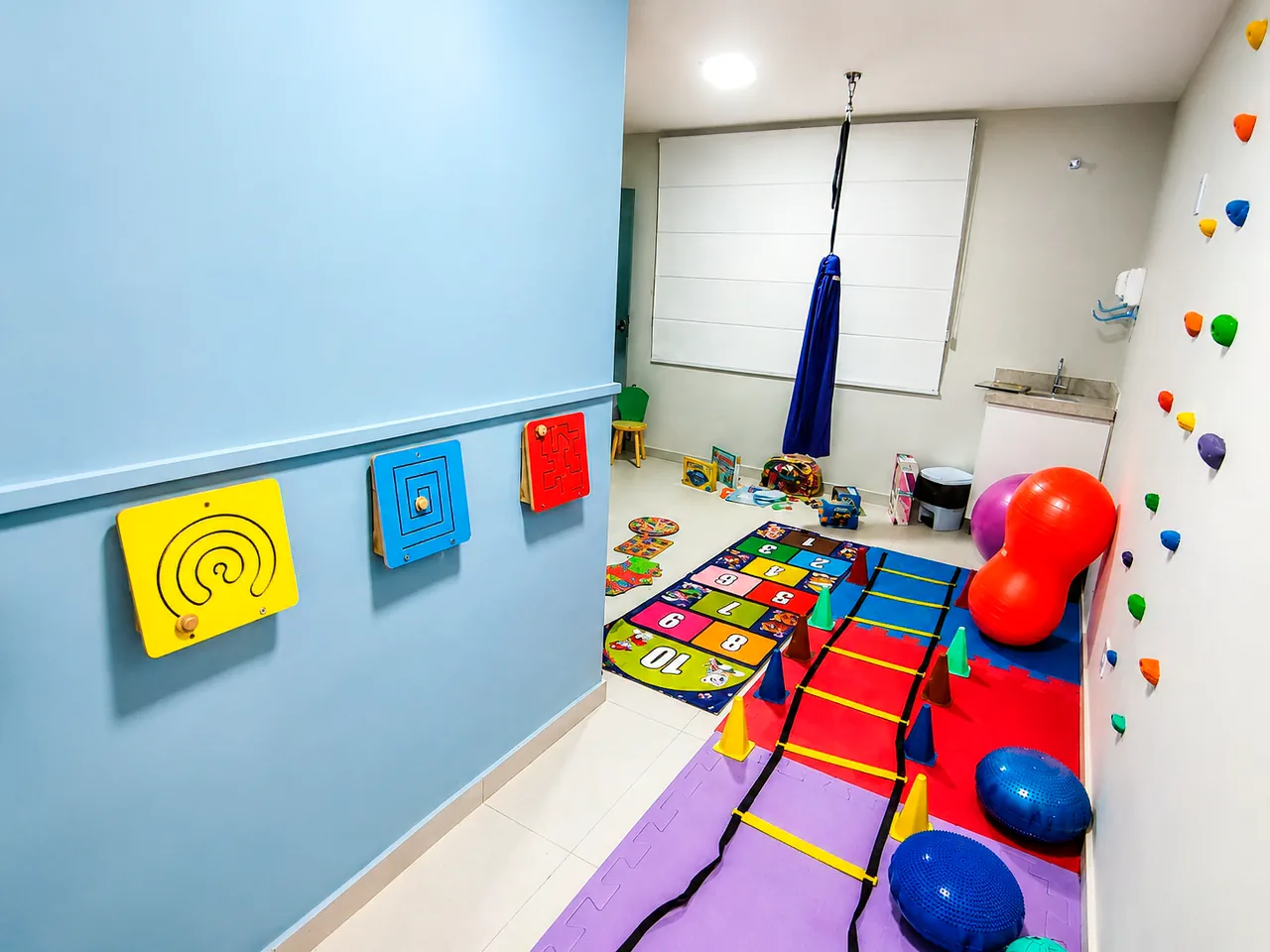 Sala de integração sensorial com painéis, balanço e tatames coloridos